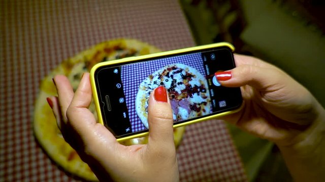 People and food concept. Young woman in a restaurant make photo of food with mobile phone camera