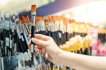 Male artist hand choosing artistic paintbrushes. New paint brushes on shelf display in stationery...