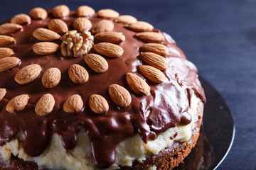 Homemade chocolate cake with milk cream and almonds on black wooden background.