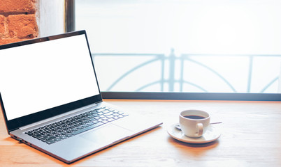 Open laptop and cup of coffee on the table in the cafe, mock up, freelance concept