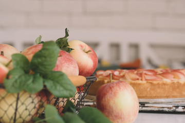 Ripe organic apples in vintage basket on rustic white table. Apple cheesecake in the background. Summer homemade apple tart with ingredients. Healthy organic food. Tasty breakfast.
