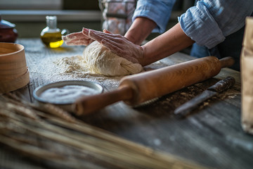 Baking concept. Working woman prepares pastry by himself, kneads dough on wooden counter with flour and rolling pin. Female cook bakes bread or delicious bun.