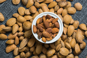 Peeled almonds in a white bowl on grey fabric texture. Nuts flat lay.