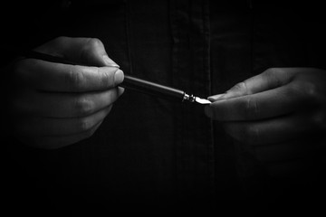 female hand elegantly holding an ink pen with a metal tip close-up on a black background. classic...