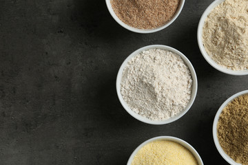 Bowls with different types of flour on grey background, top view. Space for text