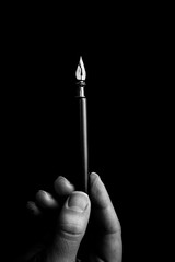 female hand elegantly holding an ink pen with a metal tip close-up on a black background. classic fountain pen isolated macro black and white. copy space. vertical