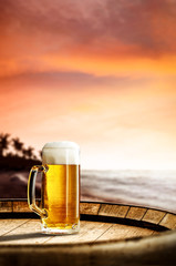 Cold fresh beer on barrel of wood. Summer sunset time. Sea landscape with beach and palms. Free space for your bottle. 