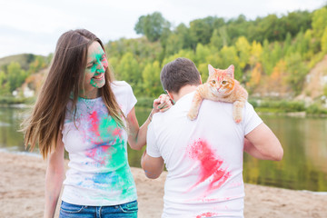 Obraz premium Festival holi, tourism and nature concept - Portrait of woman and man with cat covered multi-colored dust