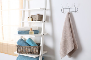 Fototapeta na wymiar Shelving unit and rack with clean towels and toiletries near white wall