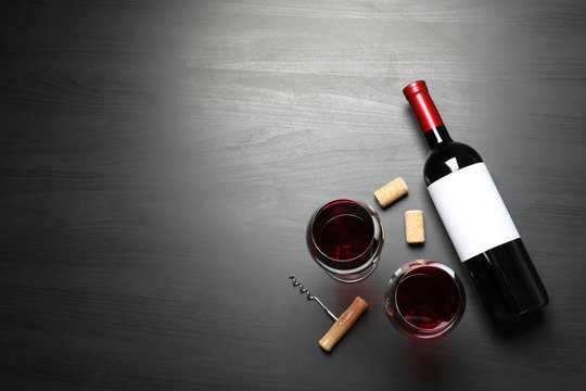 Glasses and bottle with red wine on dark background, flat lay. Space for text