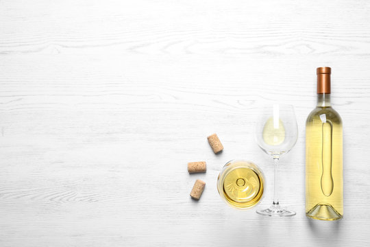 Glasses and bottle with white wine on wooden background, flat lay. Space for text