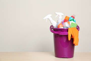 Bucket with cleaning supplies on table against grey background. Space for text
