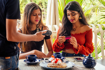 female Customer paying for coffee, pancakes with credit card sitting with laptop online shopping black friday sale.the waiter payment terminal while client doing contactless purchase in cafe