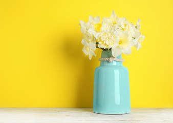 Bouquet of daffodils in vase on table against color background, space for text. Fresh spring flowers