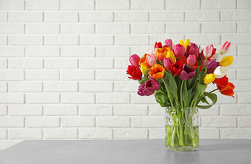 Vase with beautiful spring tulip flowers on table near brick wall. Space for text