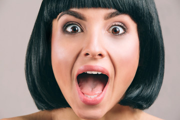 Young woman with black hair posing on camera. Emotional young brunette screaming. Bob haircut. Short black hair. Young woman isolated on light studio background.