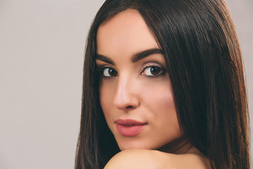 Young woman with long black hair posing on camera. Close up portrait of beautyful model looking straight. Nice features. Isolated on light background.