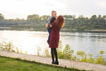 Motherhood and children concept - young mother with son in her arms near the river