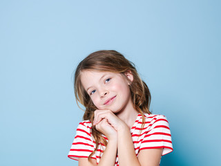 pretty girl with curly hair and red white striped shirt is posing in front of blue background and is happy