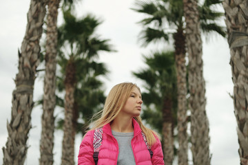 Portrait of beautiful blond girl posing for photo at the park with palm tree