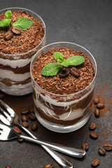 two portions Classic tiramisu dessert in a glass on dark concrete background
