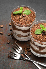 two portions Classic tiramisu dessert in a glass on dark concrete background