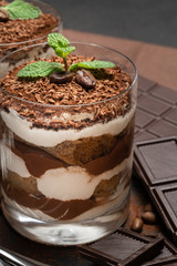 two portions Classic tiramisu dessert in a glass and chocolate bar on dark concrete background