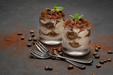 two portions Classic tiramisu dessert in a glass on dark concrete background