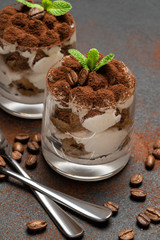 two portions Classic tiramisu dessert in a glass on dark concrete background