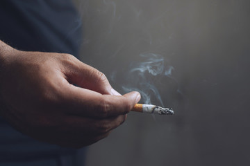 man holding smoking a cigarette in hand. Cigarette smoke spread. dark background