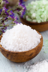 Sea salt in bowl, aroma oil in bottles, Wellness and flowers on grey textured background and flowers on vintage wooden background. Selective focus.