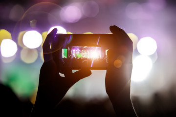 Shoots an instagram video on a mobile phone at a concert