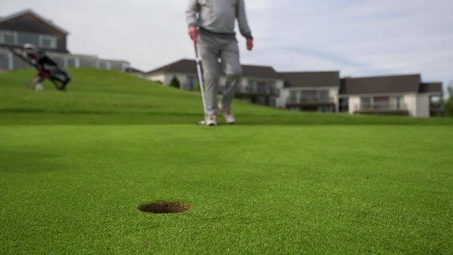 Professional golfer putting ball into the hole and missing. Golf ball by the edge of hole with player feet in background on a sunny day.