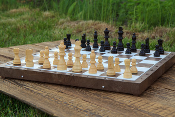 Chess board with chess pieces on wooden desk and green grass.