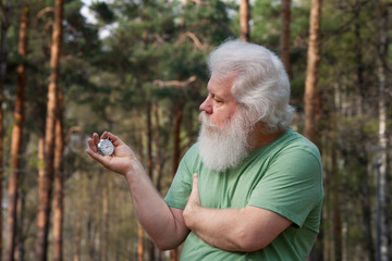 Senior sportive man looking at watchstop. Outdoor lifestyle portrait against natural tree background. Active leisure.