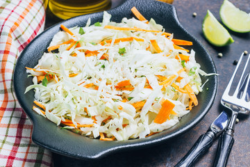 Fresh coleslaw salad in black plate on dark background.