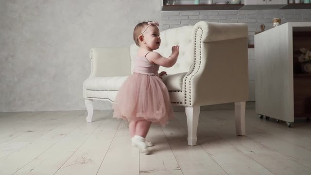 Small baby toddler girl in tutu skirt and dress near the sofa learns to walk