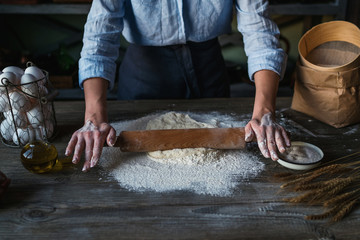 Homemade raw pastry on a wooden table on a rustic wooden surface with a rolling pin, flour, butter, wheat spikelets.
