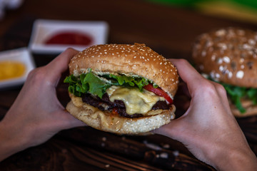 Woman holding cheeseburger. Young girl holding in hands fast food burger, american meal. Beef burger in hands with french fries on rustic wooden board. Selective focus. Toned image with copy space.