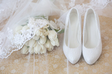 Wedding bouquet of white tulips covered with a veil next to the bride's white high heel shoes