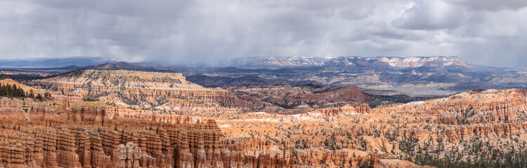 Panoramic view of a vast landscape in the American southwest. Snow capped mountain peaks in the distance and incredible red rock formations, hoodoos, in Bryce Canyon National Park, Utah. 