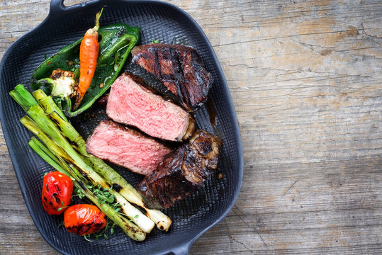 Barbecue dry aged wagyu entrecote beef steak with vegetable and herbs as top view on a gray cast iron pan with copy space right