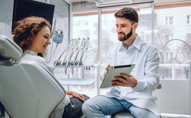 Menschen, Medizin, Stomatologie und Gesundheitskonzept - glücklicher männlicher Zahnarzt, der der Patientin im Büro der Zahnklinik Tablet-Computer zeigt.
