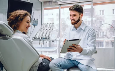Abwaschbare Fototapete Zahnärzte Menschen, Medizin, Stomatologie und Gesundheitskonzept - glücklicher männlicher Zahnarzt, der der Patientin im Büro der Zahnklinik Tablet-Computer zeigt.