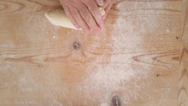 Mani di uno chef stanno preparando la pasta fatta in casa su un tagliere di legno con farina di semola e integrale.