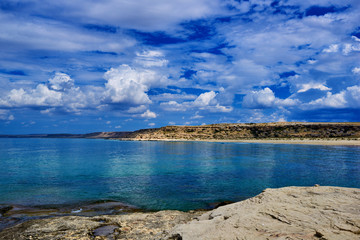 Rocky coastline with a cove and rock, split view above water surface, Mediterranean sea, Spain. Azure sea, wave and blue sky. Seascape with sea horizon and cloudy deep blue sky. Ecological tourism