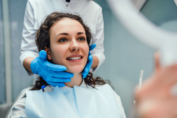 Young woman looking in mirror at dentist's office. Close up view.