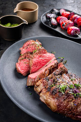 Barbecue dry aged wagyu tri tip steak sliced with hot sauce and tomato onion skewer as closeup on a modern design cast iron plate