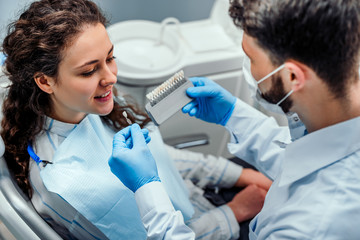 Young beautiful women in dentist chair, check and select the color of the teeth. Close up view.