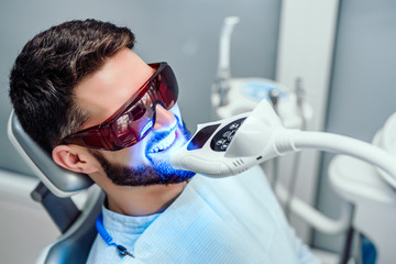 Dentist starting teeth whitening procedure with young man. - obrazy, fototapety, plakaty